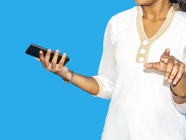 Close up of a young indian woman hand pointing finger as touching screen, isolated on blue background. With mobile phone in the other hand