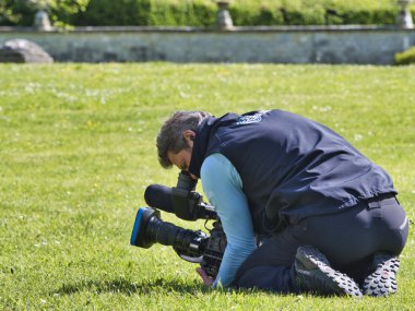 Yüksek çözünürlüklü dijital video kamera arka açı görünümü hangi kayıt veya tv ticari üretim çekim. Kameraman yerde oturan, çim.