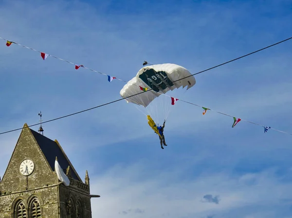 El paracaídas rojo está en el increíble cielo azul. El paracaidista militar aterriza con una gran bolsa en SAINTE MERE L 'EGLISE, FRANCIA, Normandía —  Fotos de Stock