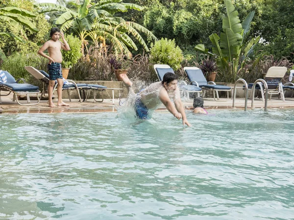 Tres hermanos adolescentes felices y su hermana están saltando a la piscina infinita en el complejo — Foto de Stock