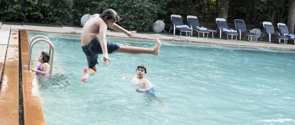 Tres hermanos adolescentes felices y su hermana están saltando a la piscina infinita en el complejo — Foto de Stock
