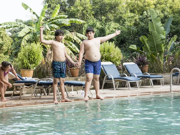 Dos felices hermanos adolescentes están saltando a la piscina infinita en el complejo — Foto de Stock