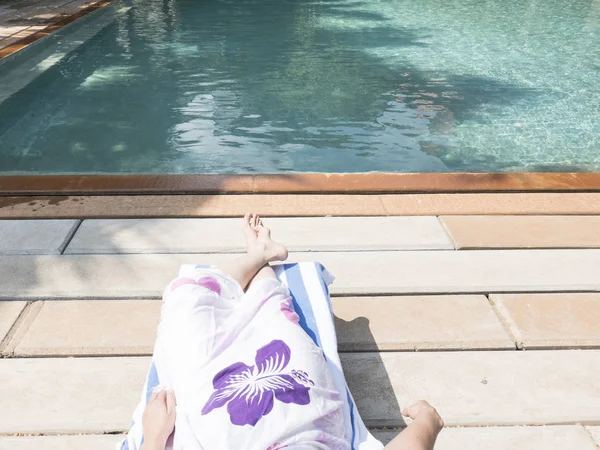 Pés descalços de jovem deitada na espreguiçadeira tomando banho de sol na piscina . — Fotografia de Stock