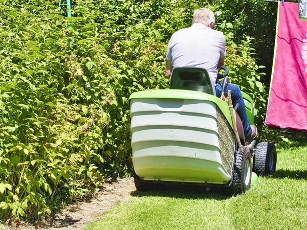 Senior man het rijden van een tractor grasmaaier in tuin met bloemen — Stockfoto