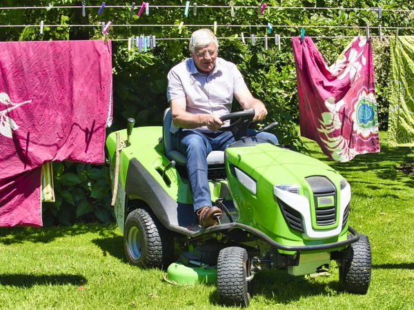 Senior man het rijden van een tractor grasmaaier in tuin met bloemen — Stockfoto