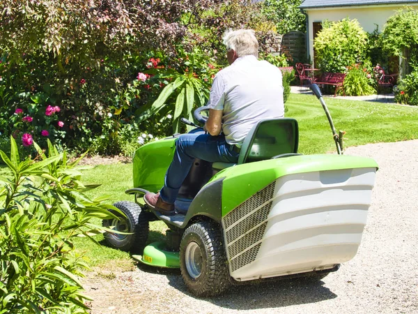 Senior fährt mit Traktor Rasenmäher in Garten mit Blumen — Stockfoto