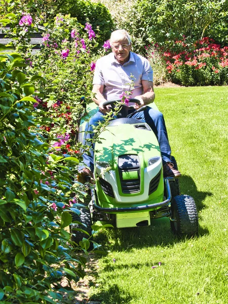 Senior man het rijden van een tractor grasmaaier in tuin met bloemen — Stockfoto