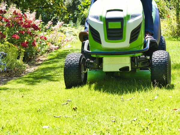 Senior fährt mit Traktor Rasenmäher in Garten mit Blumen — Stockfoto