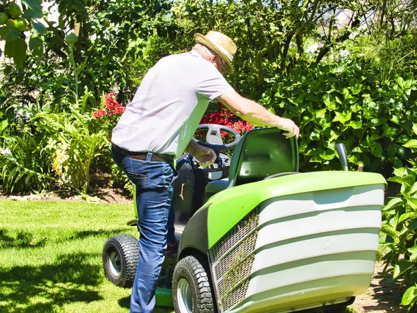 Senior man het rijden van een tractor grasmaaier in tuin met bloemen — Stockfoto