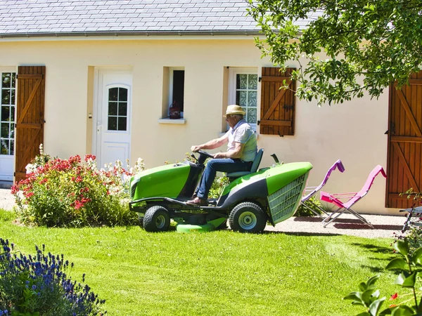 Uomo anziano alla guida di un trattore tosaerba in giardino con fiori — Foto Stock