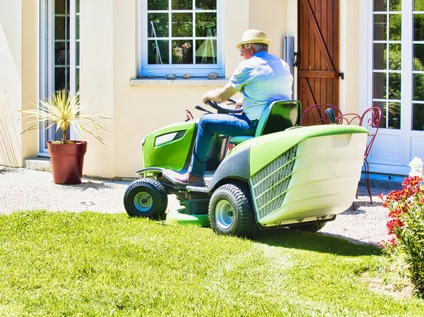 Senior man het rijden van een tractor grasmaaier in tuin met bloemen — Stockfoto