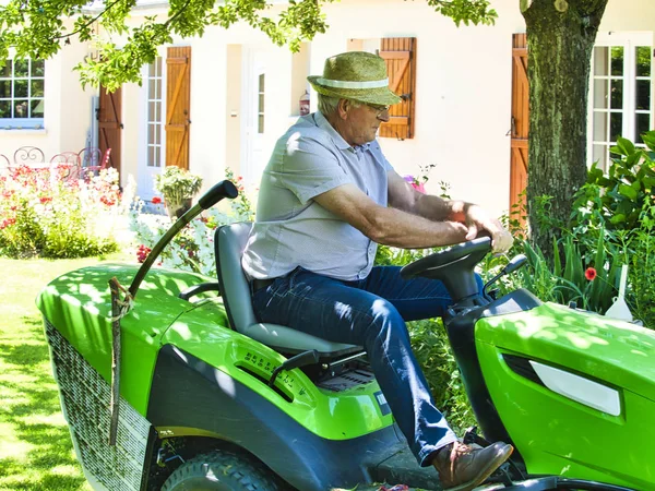 Senior man het rijden van een tractor grasmaaier in tuin met bloemen — Stockfoto