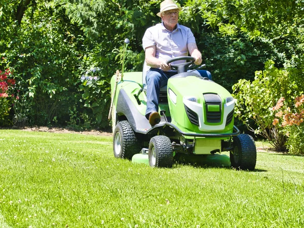 Senior man het rijden van een tractor grasmaaier in tuin met bloemen — Stockfoto