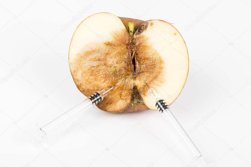 Close up Boring trace of a codling moth Cydia Pomonella, in a half wormy apple. On white background. With syringe. Concept non organic and genetically modified organism