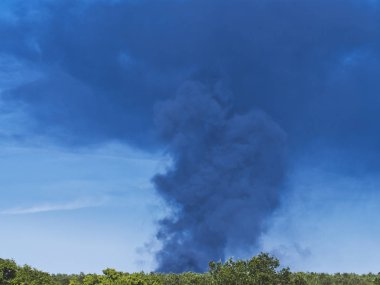 Yanan plastik geri dönüşüm yeri, gökyüzü mavisi bir yaz gününde büyük bir karanlık, siyah kalın duman yığınına neden olur. Tehlike, keder. Terörist saldırı veya patlama.