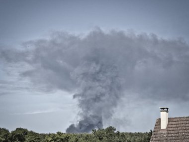 Yanan plastik geri dönüşüm yeri, gökyüzü mavisi bir yaz gününde büyük bir karanlık, siyah kalın duman yığınına neden olur. Tehlike, keder. Terörist saldırı veya patlama.