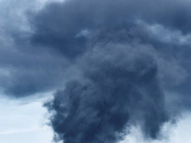 Yanan plastik geri dönüşüm yeri, gökyüzü mavisi bir yaz gününde büyük bir karanlık, siyah kalın duman yığınına neden olur. Tehlike, keder. Terörist saldırı veya patlama.