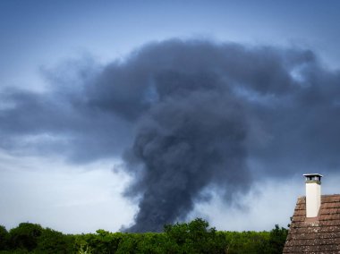 Yanan plastik geri dönüşüm yeri, gökyüzü mavisi bir yaz gününde büyük bir karanlık, siyah kalın duman yığınına neden olur. Tehlike, keder. Terörist saldırı veya patlama.