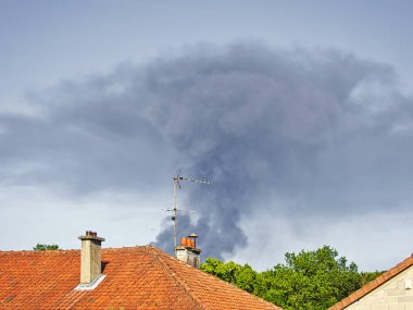 Yanan plastik geri dönüşüm yeri, gökyüzü mavisi bir yaz gününde büyük bir karanlık, siyah kalın duman yığınına neden olur. Tehlike, keder. Terörist saldırı veya patlama.