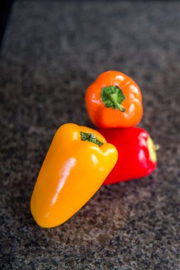 Küçük sarı turuncu kırmızı tatlı biber mutfakta siyah arka planda, kesilmeye hazır.