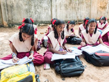 PUDUCHERRY, İNDİA - Aralık 2018. Tanımlanamayan bir grup çocuk devlet okulu üniformalı sınıf arkadaşları yerde oturup açık havada kitaplarla çalışıyorlar..