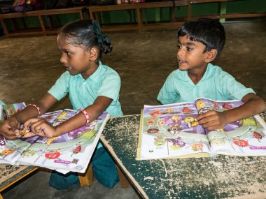 PUDUCHERRY, İNDİA - Aralık 2018. Tanımlanamayan mutlu öğrenciler devlet okulu üniformalı sınıf arkadaşları kapalı alanda İngilizce kitapları okuyorlar. Yardım için gülümseyen zavallı gençlerin portresi..