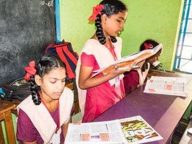 PUDUCHERRY, İNDİA - Aralık 2018. Tanımlanamayan, devlet okulu üniformalı, sandalyeye oturmuş kapalı alanda kitap okuyan ciddi sınıf arkadaşları. Okul gençlerinin portresi.