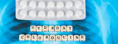 Roman Covid-19, Coronavirus. Enfekte olmuş akciğerler radyoloji mavi görüntü arka planı, üzerinde beyaz haplar var. Tahta harflerle yazılmış hidroksi kloroksin..