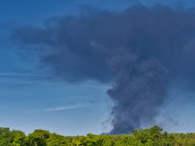 Yanan bir plastik geri dönüşüm yeri, gökyüzü mavi yaz gününde koyu siyah bir duman yığınına neden olur. Tehlike, keder. Terörist saldırı ya da patlama. Çevre felaketi