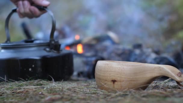 Hälla te från en tekanna i en trä mugg bredvid elden. — Stockvideo