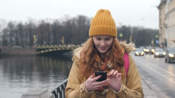 Студентка гуляет по осеннему городу и пишет смс на телефон — стоковое видео