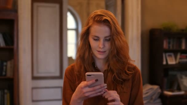 Jeune femme caucasienne cheveux rouges marchant SMS téléphone intelligent dans le café — Video