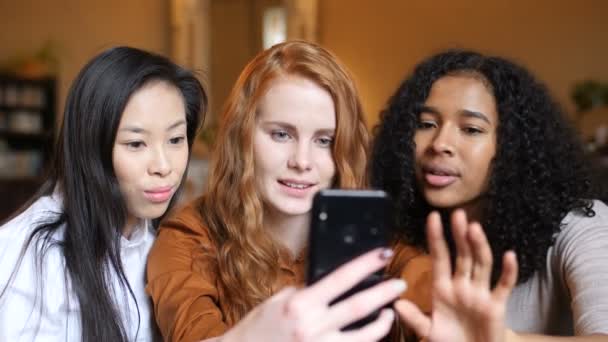 Groupe multi ethnique de filles riant à un téléphone, une tablette ensemble dans un café — Video