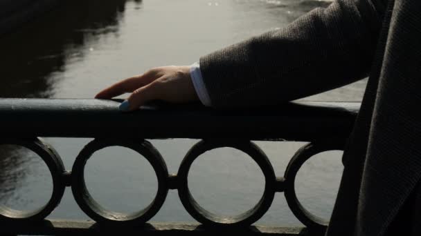 Елегантна жіноча рука торкається перил старого мосту через річку в місті. дівчина гуляє в сонячний вечір — стокове відео