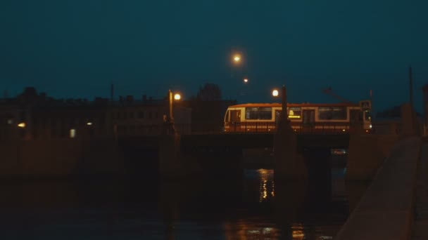 Miejskie przejażdżki tramwajem w nocy na moście w starym mieście. Światła na mostku połysk żółty. — Wideo stockowe