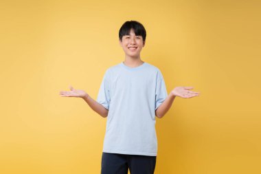 Asyalı bir çocuk geniş bir gülümsemeyle sarı bir zemine uzanır.