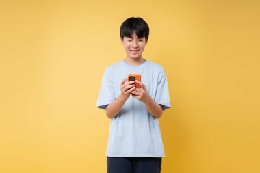 Genç, parlak sarı bir stüdyoda turuncu bir akıllı telefonla konuşurken mutlu mesut odaklanır.