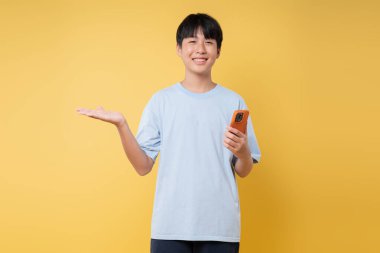 Genç insan elini açıp gülümseyerek sarı bir zemin üzerinde cep telefonu tutuyor.