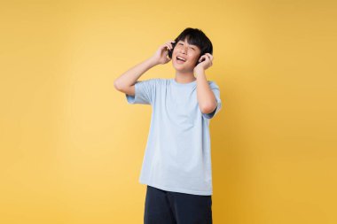 Parlak sarı bir arkaplan önünde kulaklıklı neşeli bir genç.