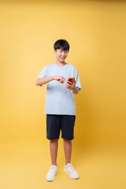 Genç bir insan, günlük kıyafetler giyen, sıcak sarı bir arkaplan karşısında akıllı telefonuyla etkileşime giriyor.