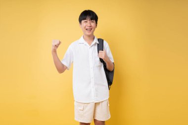 Gülümseyen bir öğrenci sınıfa beyaz gömlek ve haki rengi şortla girmeye hazır.