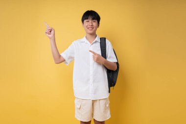 Bir öğrenci gülümsüyor ve okula gitmeye hazırlanıyor. Stüdyoda sırt çantası takıyor.