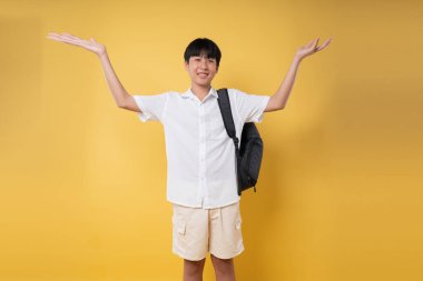 Kolları açık ve sırt çantalı mutlu bir öğrenci canlı sarı bir zemin üzerinde duruyor okula geri dönüyor.