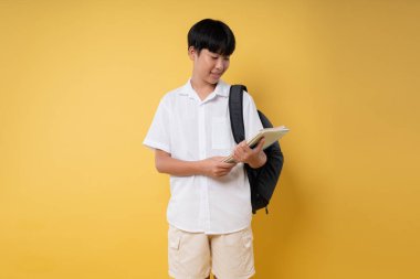 Sırt çantası ve sarı arka planda not defteriyle gülümseyen genç öğrenci öğrenmeye hazır.