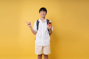 Beyaz yakalı ve haki şortlu genç bir öğrenci sarı arka planda akıllı bir telefonla işaret ediyor.