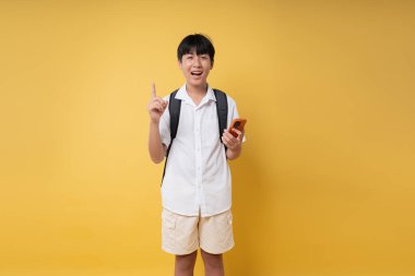 Gülümseyen bir öğrenci, canlı sarı bir arkaplanda elinde telefonla neşeli bir şekilde dikiliyor.