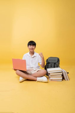 Sırt çantalı ve dizüstü bilgisayarlı gülümseyen öğrenci sarı arka planda başarı başarısı elde etti.