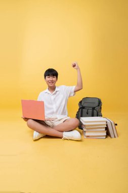 Gülümseyen genç bir öğrenci dizüstü bilgisayarı ve sırt çantasıyla mutlu bir şekilde oturuyor.