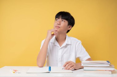 Beyaz bir masada, açık bir defterle düşünceli bir öğrenci ve sarı arkaplana karşı kitapları istiflemiş.