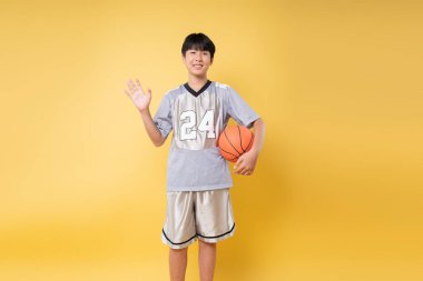 Basketbol kıyafetli genç bir çocuk elinde parlak bir arka planla neşeyle poz veriyor.